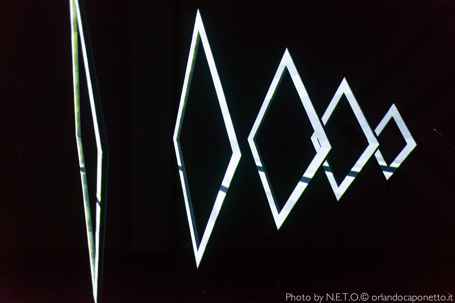 Sculture luminose a forma di rombo di diverse dimensioni su sfondo scuro.