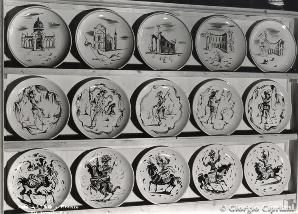 Piatto decorato con disegni di edifici e figure storiche, esposti su uno scaffale in legno.